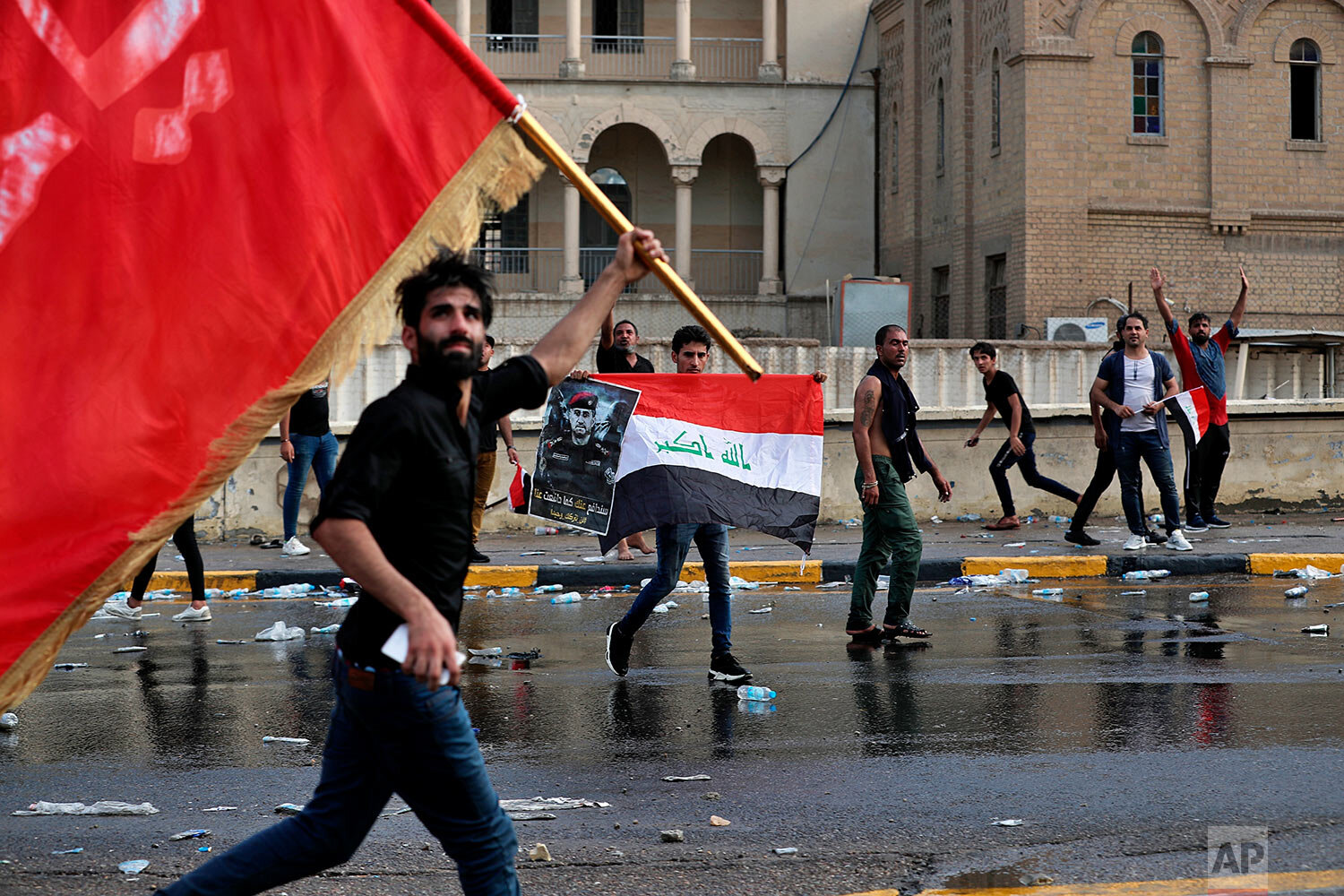 Protestors wave flags and hold a poster of Lt. Gen. Abdul-Wahab al-Saadi during a protest in Tahrir Square, in central Baghdad, Iraq, Tuesday, Oct. 1, 2019. Spontaneous rallies, which began Tuesday, started as mostly young demonstrators took to the streets demanding jobs, improved services like electricity and water, and an end to corruption in the oil-rich country. In a desperate attempt to curb massive rallies, authorities blocked the internet and imposed an around-the-clock curfew in the capital. (AP Photo/Khalid Mohammed)