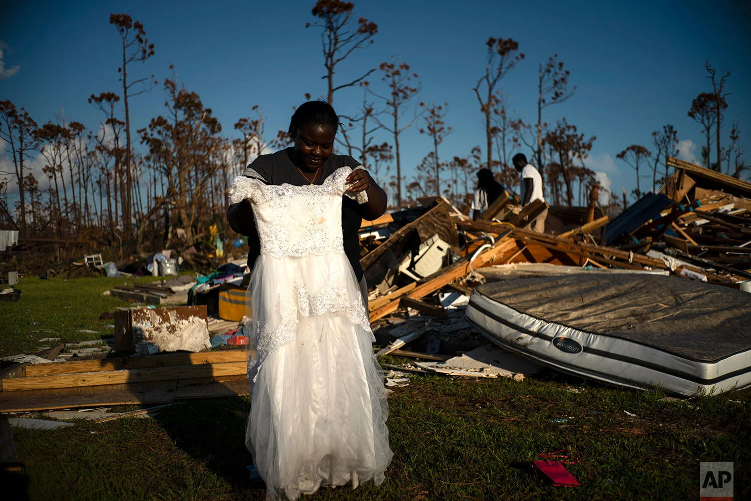 Synobia Reckley holds up the dress her niece wore as a flower girl at her wedding, as she goes through valuables in the rubble of her home destroyed one week ago by Hurricane Dorian in Rocky Creek East End, Grand Bahama, Bahamas, Sunday, Sept. 8, 2019. Synobia, 25, married two days after Hurricane Mathew in 2016, which passed over her home without doing serious damage. (AP Photo/Ramon Espinosa)