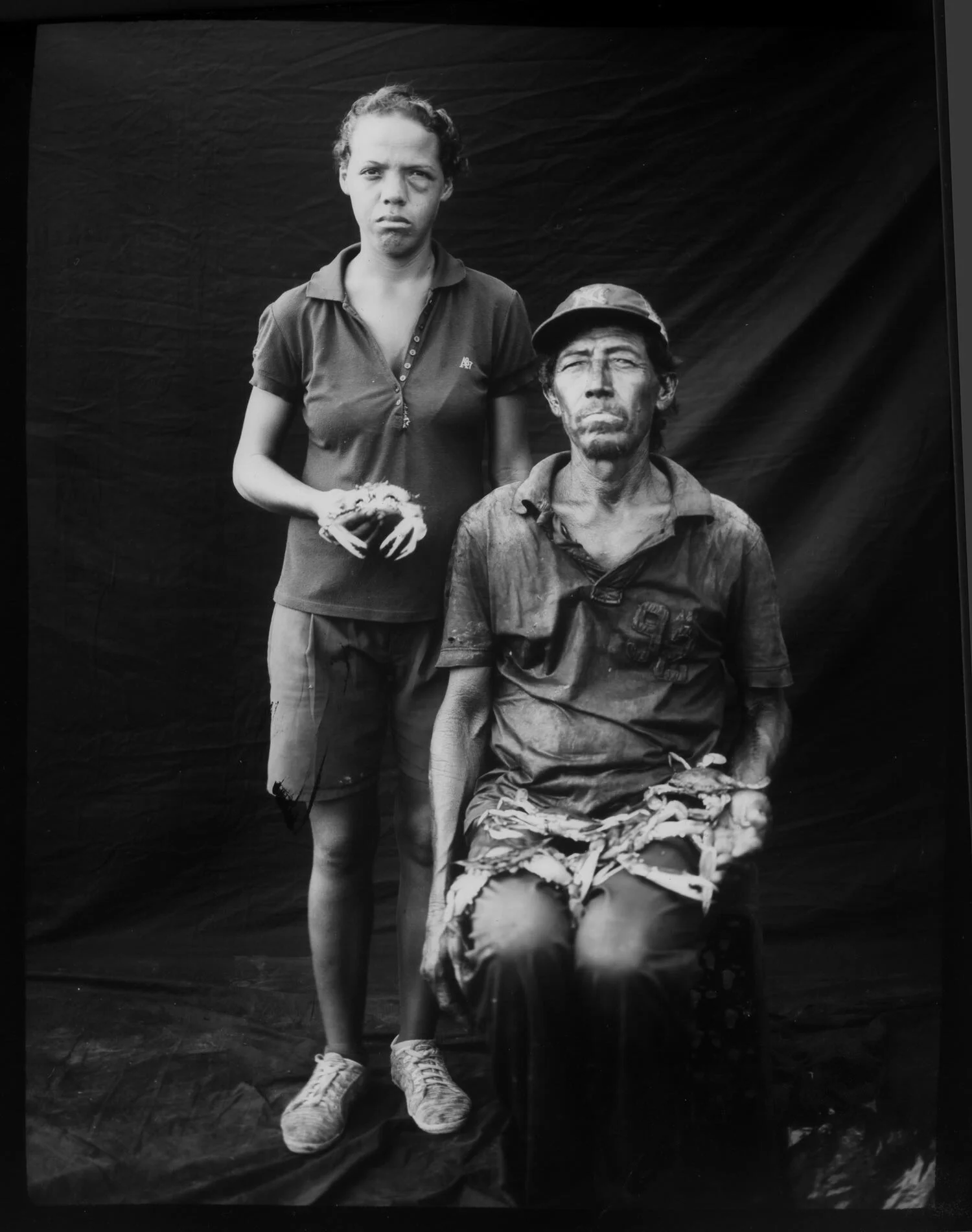 In this July 11, 2019 photo, fisherman Antonio Tello poses for the picture with her daughter Genesis Tello while cleaning oil stained crabs freshly caught by him from Lake Maracaibo, in Cabimas, Venezuela. “We have spent a lifetime of fishing, 7 years ago this lake was clean, we have to fight now with all that amount of oil. Now we just have to survive". (AP Photo/Rodrigo Abd)