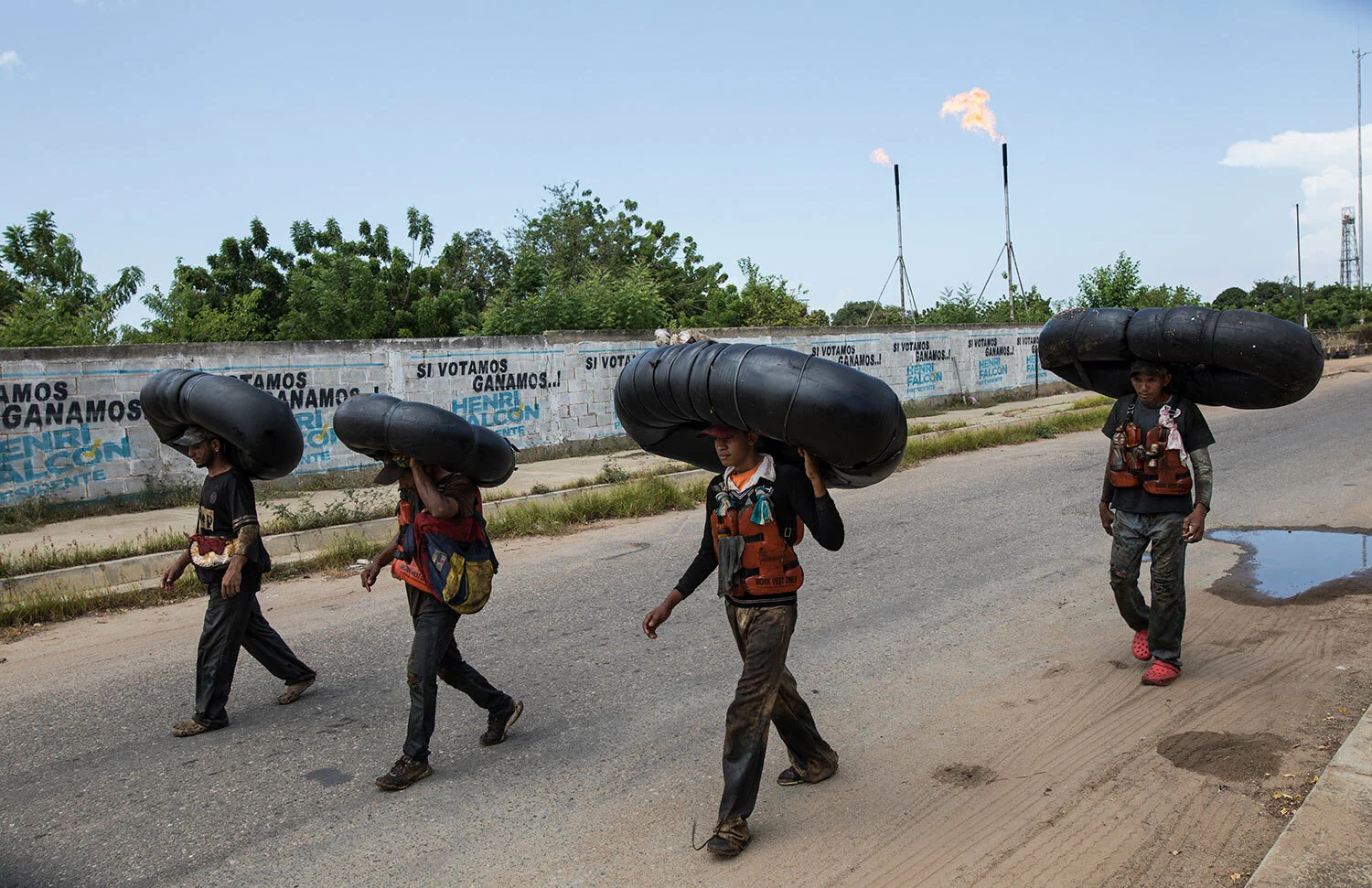 Oil-covered fishermen carry home the truck tire inner tubes they use to float on and fish from on Lake Maracaibo in Cabimas, Venezuela, July 12, 2019. (AP Photo/Rodrigo Abd)