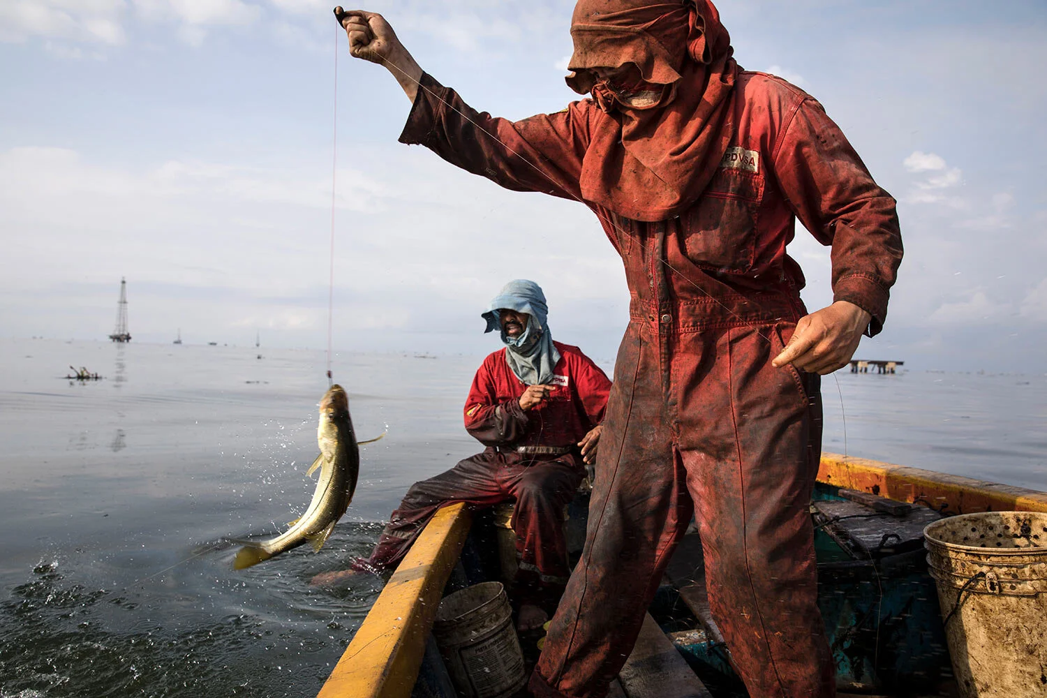 Fishermen wearing oil stained uniforms from Venezuela’s state-run oil firm PDVSA, catch bass known as "robalo" near La Salina crude oil shipping terminal, on Lake Maracaibo near Cabimas, Venezuela, May 18, 2019. (AP Photo/Rodrigo Abd)