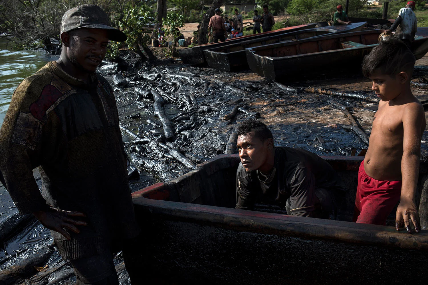 Fishermen Erick Alejandro, left, and Kelvin Alcala remove oil accumulated inside their boat after a workday on the oil-soaked shore of Lake Maracaibo in Cabimas, Venezuela, July 4, 2019. (AP Photo/Rodrigo Abd)