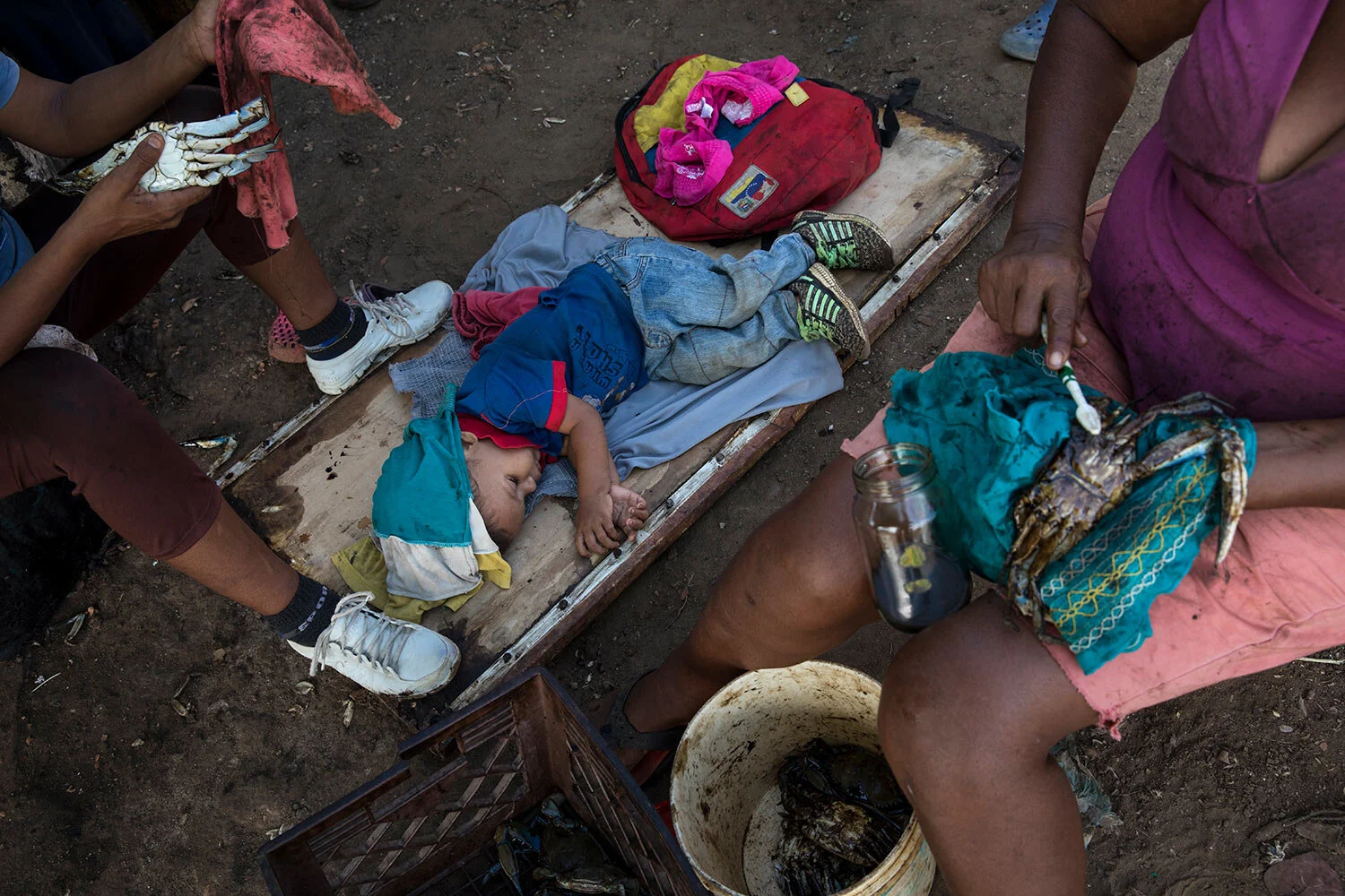 A boy sleeps as locals clean oil off of freshly harvested crabs from Lake Maracaibo, in Punta Gorda, Cabimas, Venezuela, May 21, 2019. (AP Photo/Rodrigo Abd)