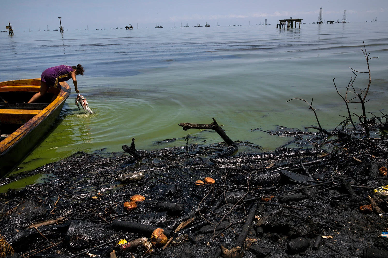 Fabiola Elizalzabal washes fish caught by her father near La Salina crude oil shipping terminal on Lake Maracaibo, next to an oil-covered shore in Cabimas, Venezuela, July 3, 2019. (AP Photo/Rodrigo Abd)