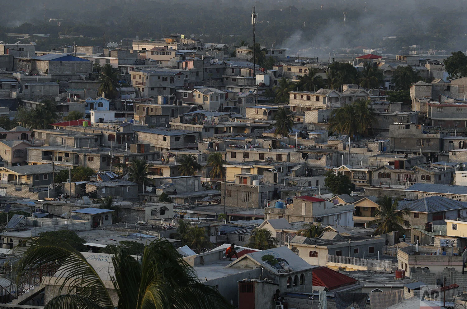 People pass the time on rooftops as afternoon turns to evening, in Port-au-Prince, Haiti, Tuesday, Oct. 8, 2019. (AP Photo/Rebecca Blackwell)