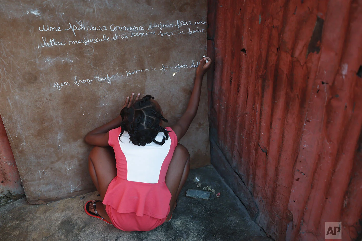 A girl writes in French and Creole on a chalkboard: "A sentence always begins with a capital letter and ends with a period," outside a one-room home in the Cite Soleil district of Port-au-Prince, Haiti, Wednesday, Oct. 9, 2019. (AP Photo/Rebecca Blackwell)