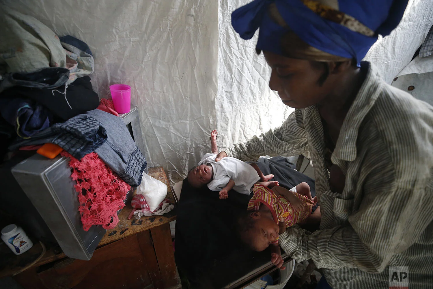 Miland Pierre, 22, tends to her 11-day-old twins Milanda and Milo who were born in the one-room shack she, her husband, and their two older children share on the edge of a waterway heavily polluted with trash and human waste in the Cite Soleil district of Port-au-Prince, Haiti, Wednesday, Oct. 9, 2019. (AP Photo/Rebecca Blackwell)