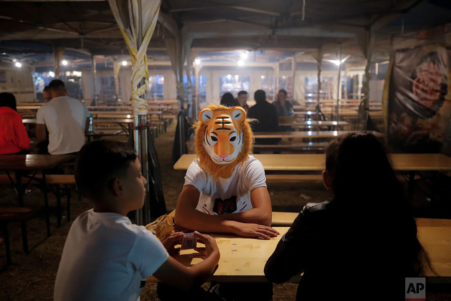 Children, one wearing a tiger mask, sit at a table in the food area of an autumn fair in Titu, southern Romania, Sept. 12, 2019. (AP Photo/Vadim Ghirda)