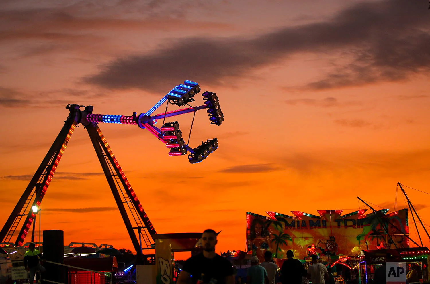 Rides are backdropped by the sunset sky at an autumn fair in Titu, southern Romania, Sept. 12, 2019. (AP Photo/Vadim Ghirda)