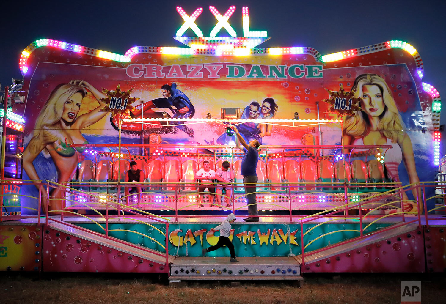 A small child runs by as a man adjusts a lights of a ride at an autumn fair in Titu, southern Romania, Sept. 12, 2019. (AP Photo/Vadim Ghirda)