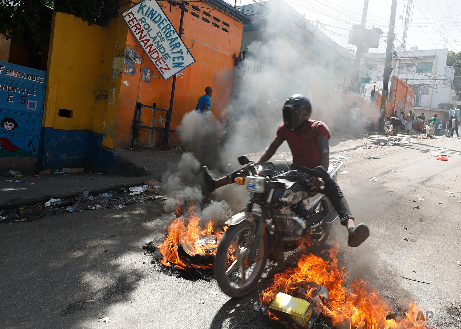 A man drives his motorcycle through a burning barricade during anti-government protests in Port-au-Prince, Haiti, Friday, Oct. 11, 2019. (AP Photo/Rebecca Blackwell)