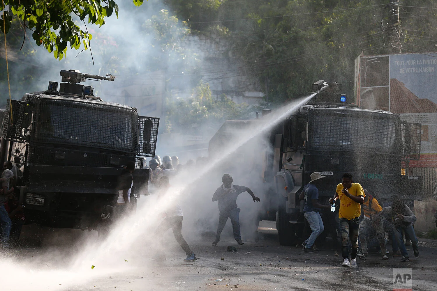 Protesters trying to break through a barricade leading toward the residence of Haitian President Jovenel Moïse flee as police fire a water cannon, in Petionville, Port-au-Prince, Haiti, Friday, Oct. 11, 2019. (AP Photo/Rebecca Blackwell)