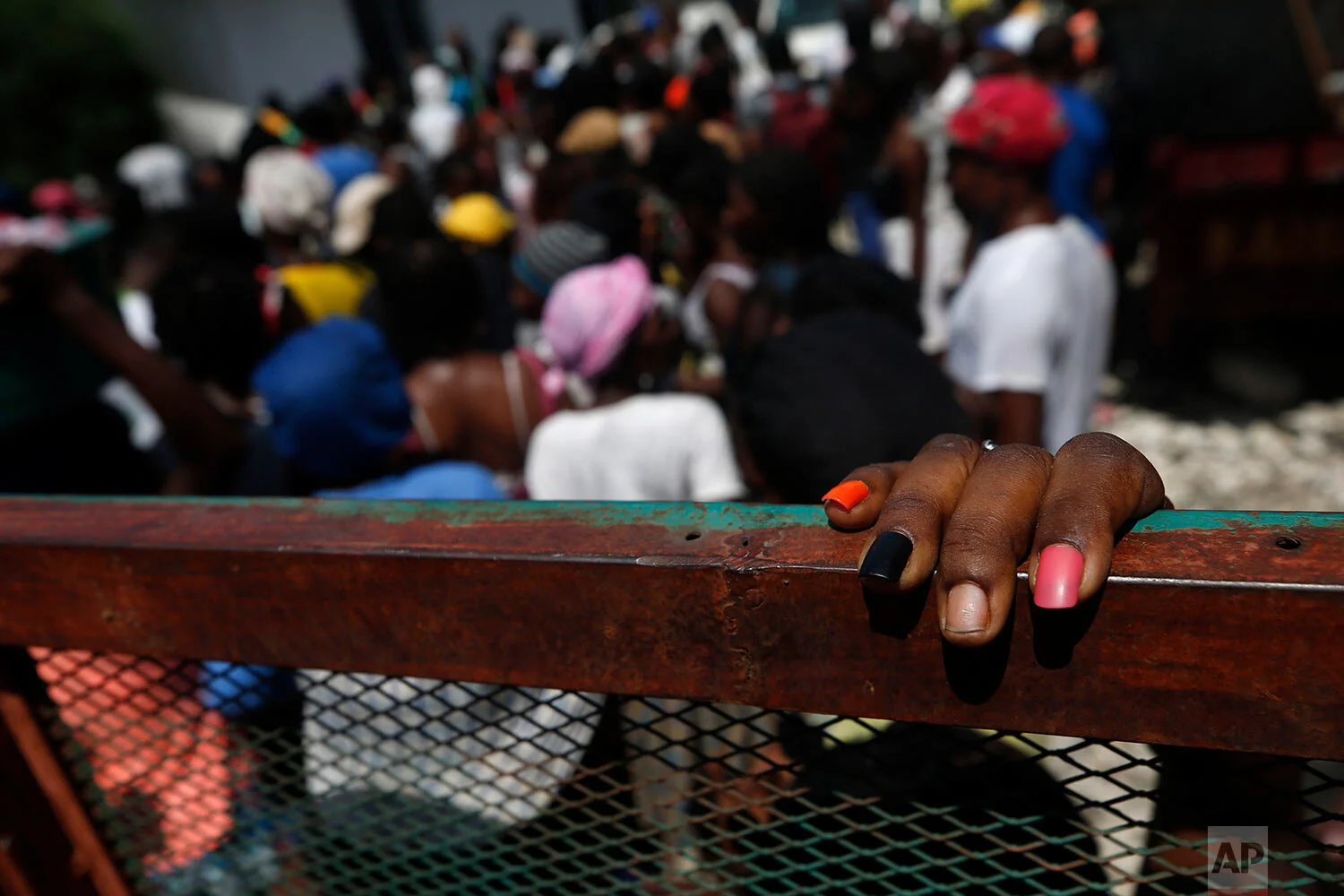 A woman with painted nails leans against a truck as people wait for distribution to restart, after a federal government hand-out of food and school supplies was temporarily suspended when the lines turned into jostling crowds, at the mayor's office in Cite Soleil, Port-au-Prince, Haiti, Thursday, Oct. 3, 2019. (AP Photo/Rebecca Blackwell)