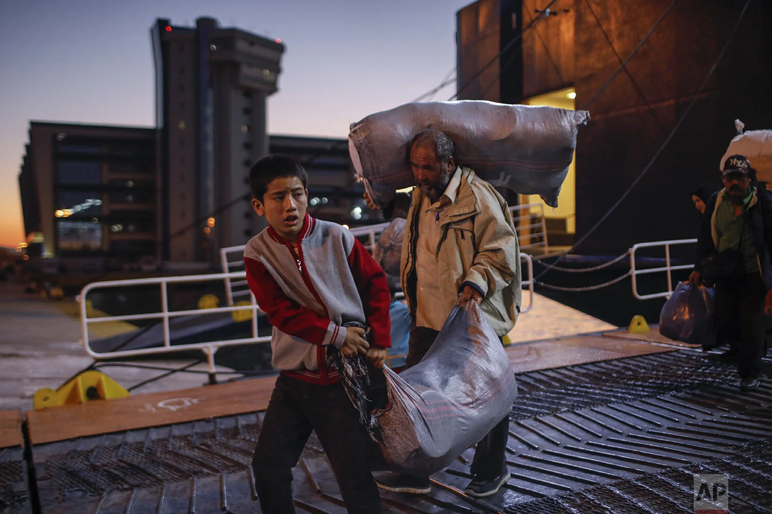 Migrants and refugees carry their belongings as they disembark from a ferry at the port of Piraeus, near Athens, Tuesday, Oct. 1, 2019. (AP Photo/Petros Giannakouris)