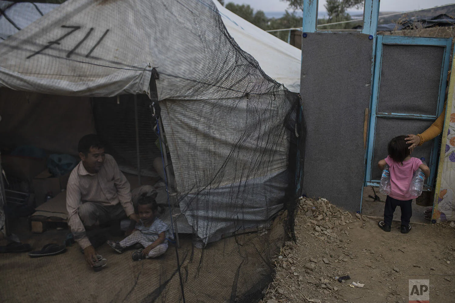 Abdul Hanoi, 38, from Afghanistan, sits next to his daughter Yesna outside their tent in a makeshift refugee and migrant camp on the fringes of the overcrowded Moria camp on the Greek island of Lesbos, Friday Oct. 4, 2019. (AP Photo/Petros Giannakouris)