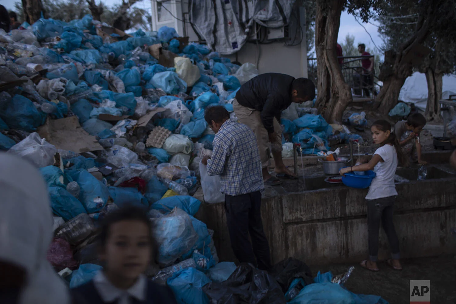 People use the public wash area, in front of a pile of garbage bags at a makeshift refugee and migrant camp next to the overcrowded Moria camp on the Greek island of Lesbos, Thursday, Oct. 3, 2019.. (AP Photo/Petros Giannakouris)