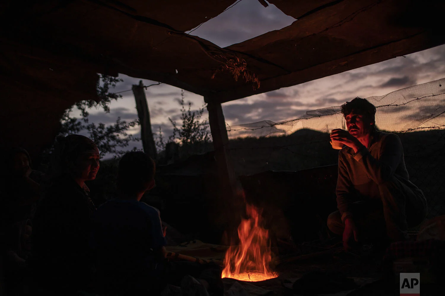 People from Afghanistan drink tea over the fire of a makeshift bakery in the overcrowded Moria refugee and migrant camp, Lesbos island, Greece, Tuesday, Oct. 8, 2019. (AP Photo/Petros Giannakouris)