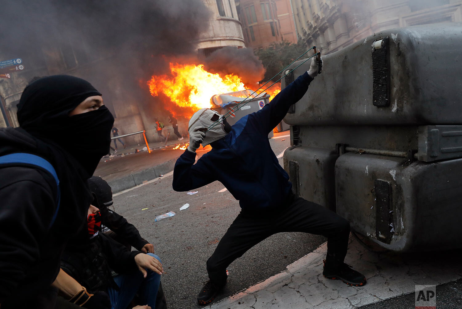 A protestors uses a sling during clashes with police in Barcelona, Spain, Friday, Oct. 18, 2019.The Catalan regional capital is bracing for a fifth day of protests over the conviction of a dozen Catalan independence leaders. Five marches of tens of thousands from inland towns are converging in Barcelona's center for a mass protest. (AP Photo/Bernat Armangue)