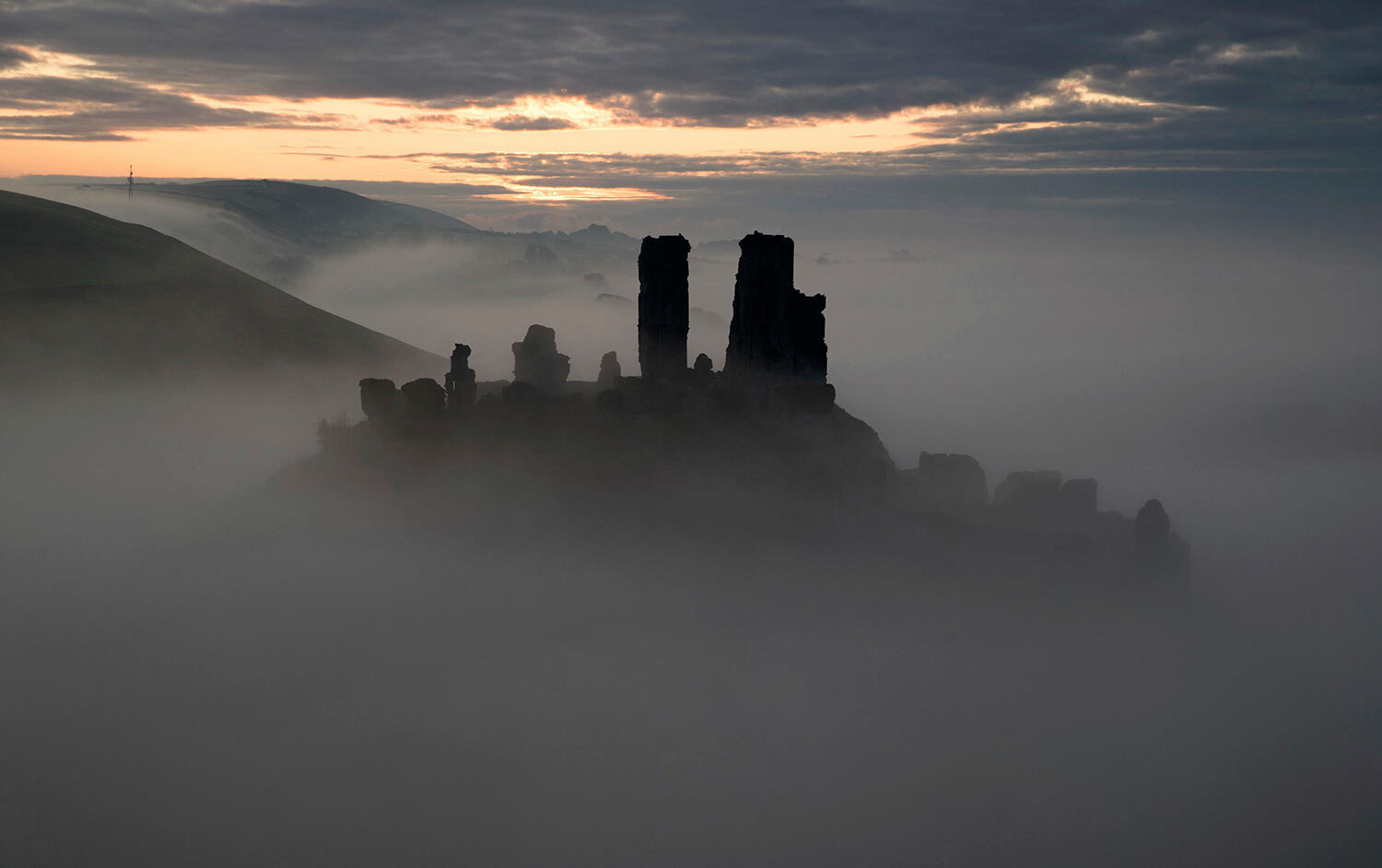 The sun begins to rise behind a mist covered Corfe Castle in Dorset, England, Tuesday, Oct. 22, 2019. (Andrew Matthews/PA via AP)