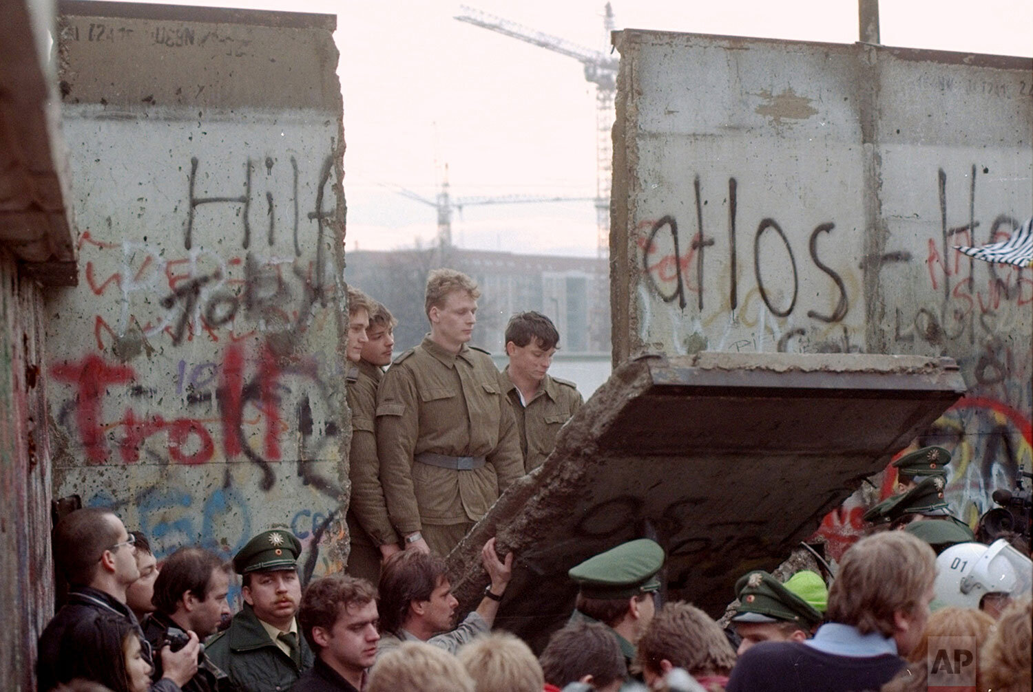  East German border guards are seen through a gap in the Berlin wall after demonstrators pulled down a segment of the wall at Brandenburg Gate, Berlin, Nov. 11, 1989. (AP Photo/Lionel Cironneau) 