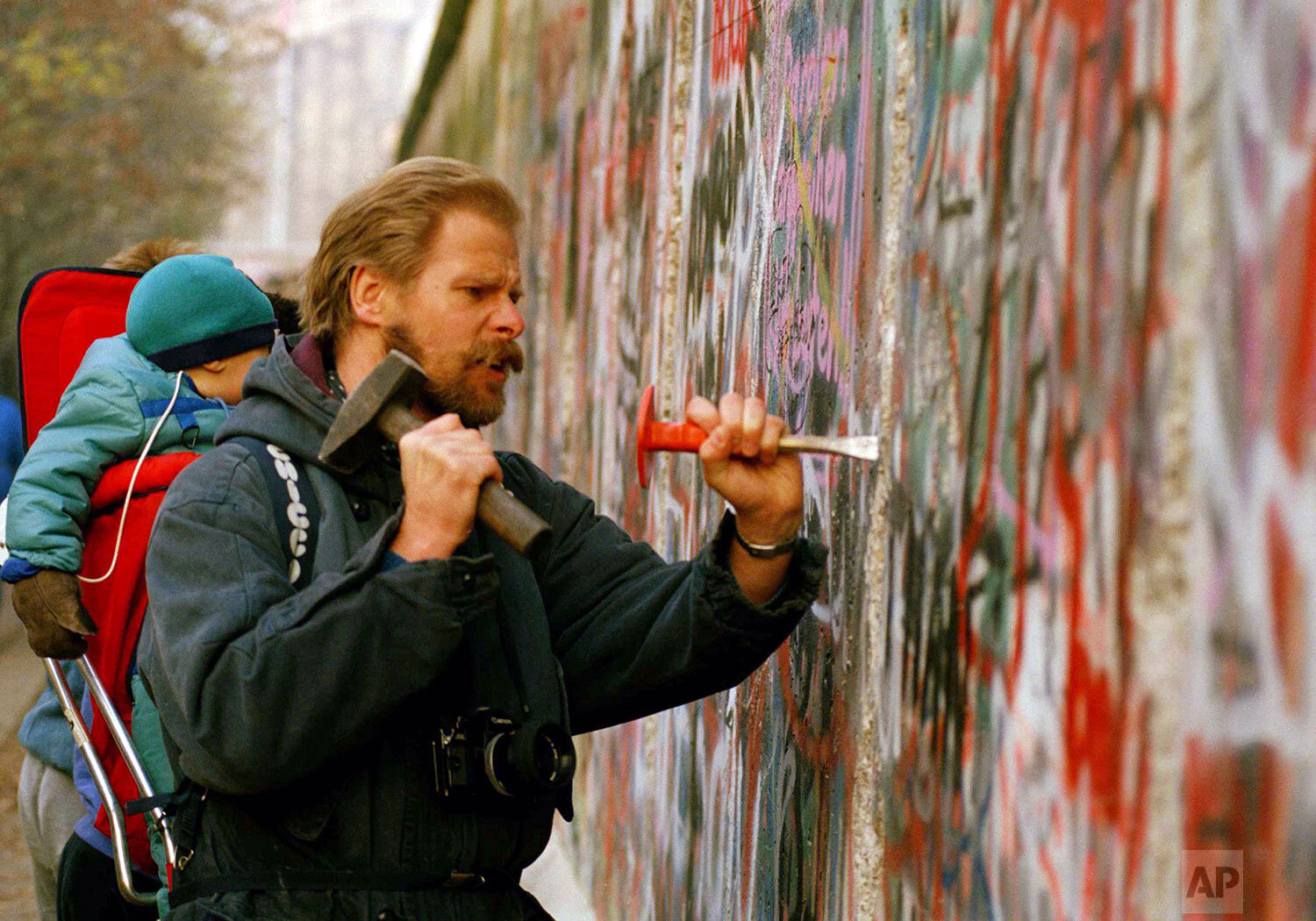  A sight-seeing West Berliner carries his baby and uses a hammer and chisel to carve out a piece of the Berlin Wall, Nov. 14, 1989. (AP Photo/Lutz Schmidt) 