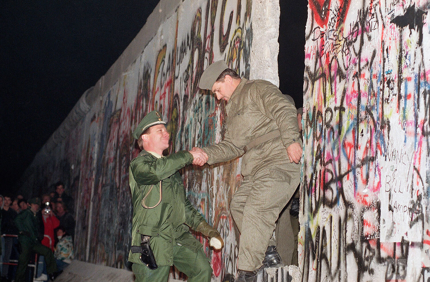  A West German policeman, left, gives a helping hand to an East German border guard who climbs through a gap of the Berlin Wall when East Germany opened another passage at Potsdamer Platz in Berlin, Nov. 12, 1989. (AP Photo/Thomas Kienzle) 