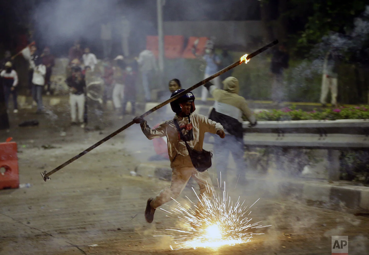 A student protester throws a burning stick at riot police officers during a clash in Jakarta, Indonesia, Monday, Sept. 30, 2019. Thousands of Indonesian students resumed protests on Monday against a new law they say has crippled the country's anti-corruption agency, with some clashing with police. (AP Photo/Achmad Ibrahim)