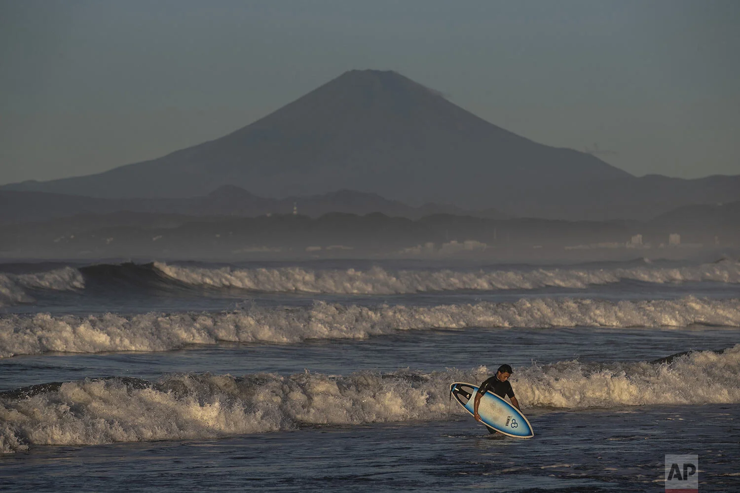 A surfer walks out of the water as Mount Fuji is visible in the distance after Typhoon Hagibis passed through the area, Sunday, Oct. 13, 2019, in Fujisawa, west of Tokyo. (AP Photo/Jae C. Hong)