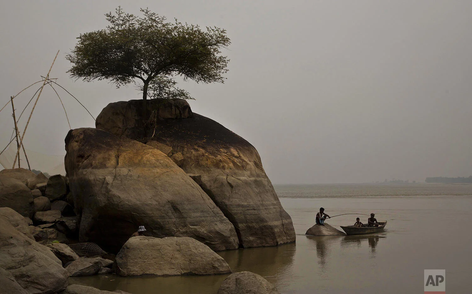 A fisherman sits on a rock to catch fish in the river Brahmaputra in Kasoshila village on the outskirts of Gauhati, India, Monday, Oct. 21, 2019. (AP Photo/Anupam Nath)