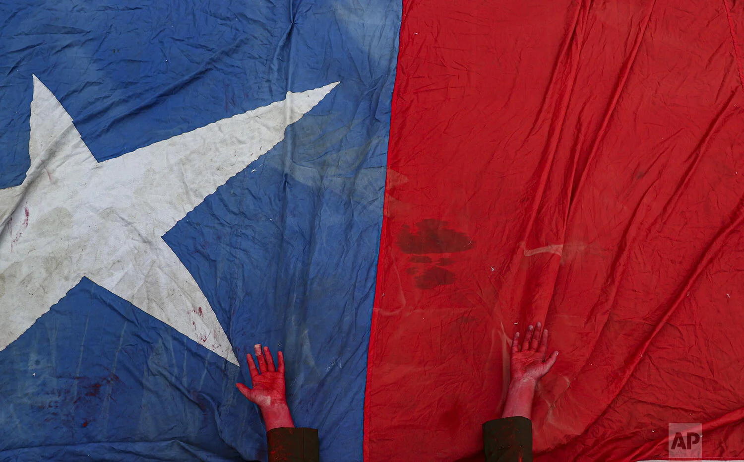 A performer places her hands, covered in red paint to symbolize blood, on a Chilean flag to honor protesters who have died amid days of demonstrations calling for better pay, pensions, schools, housing and medical care, among many other demands, during an anti-government music concert in Santiago, Chile, Sunday, Oct. 27, 2019. While most protests have been peaceful, some have devolved into riots and looting, and the government says at least 20 people have died. (AP Photo/Esteban Felix)