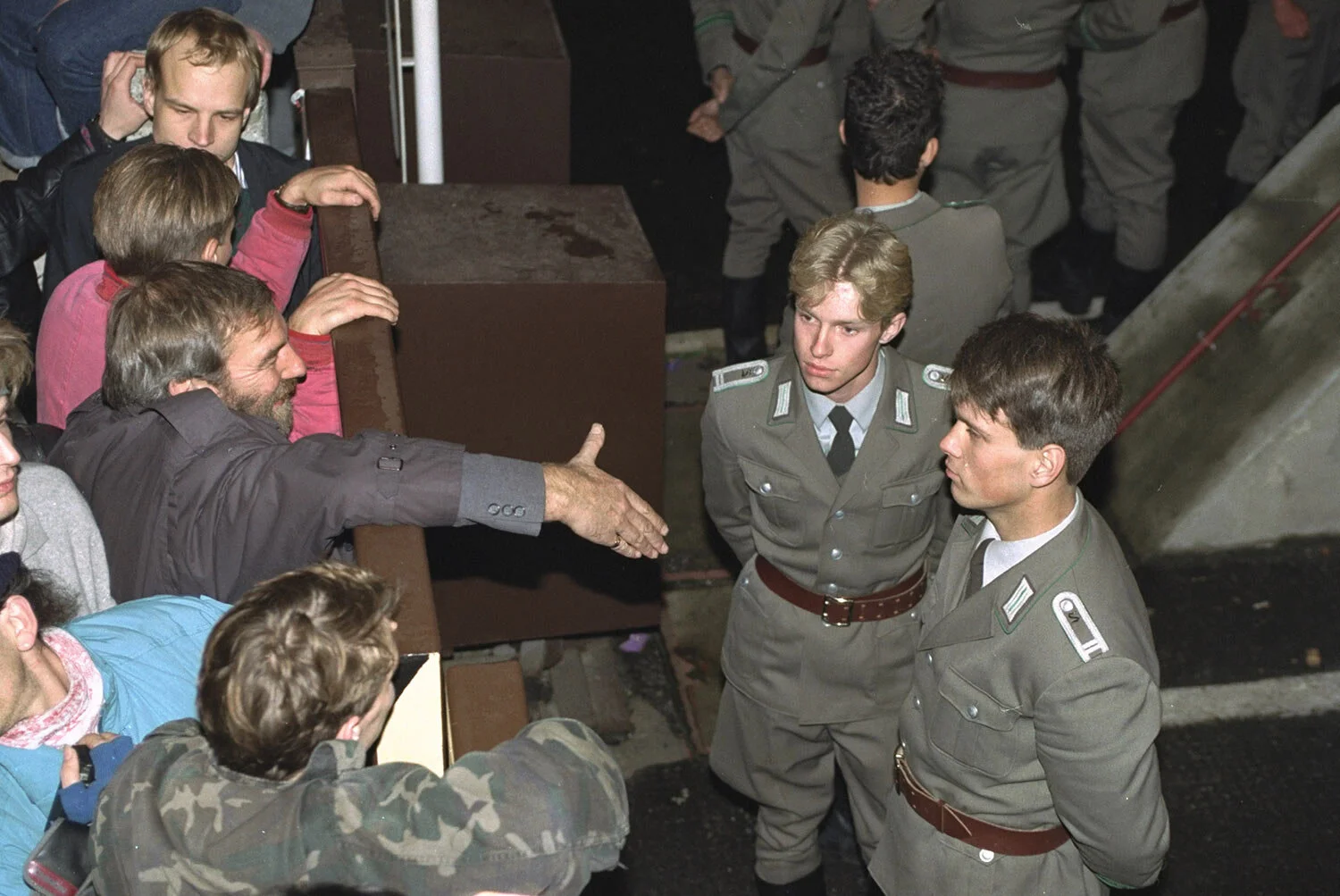 East German border policemen, right, refuse to shake hands with a Berliner who stretches out his hand over the border fence at the eastern site nearby Checkpoint Charlie border crossing point, Friday morning, November 10, 1989, after the borders were opened according to the announcement by the East German government. (AP Photo/Lutz Schmidt)
