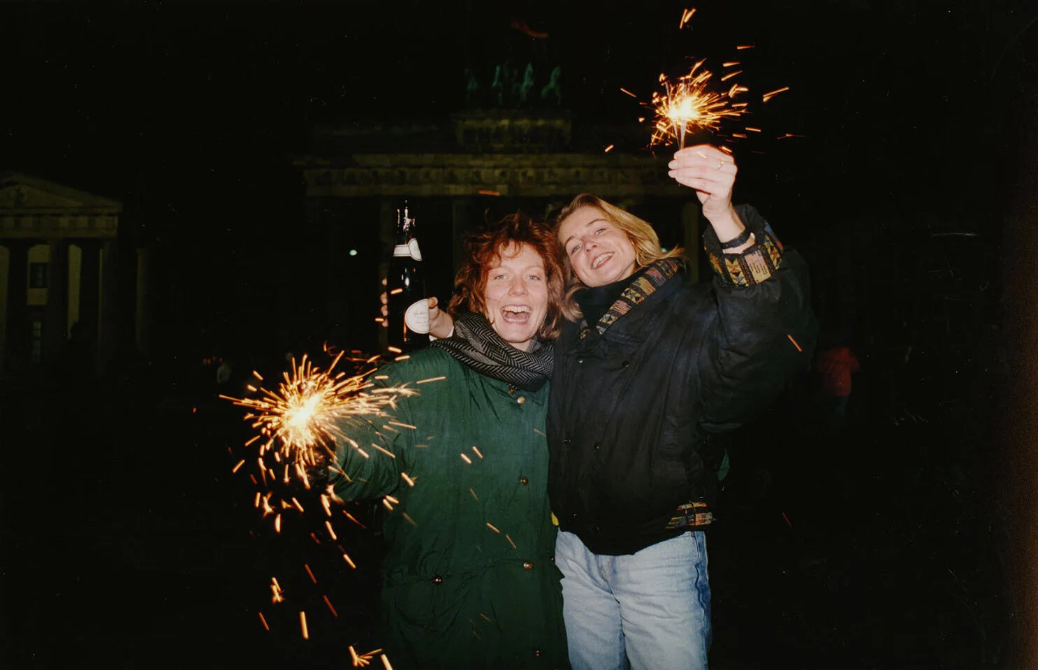 Kirsten, right, and Uta, left, from West Germany hold sparklers and a bottle of champagne as they wait on the New Year at the Brandenberg Gate, Dec. 31, 1989. Thousands of of visitors from East and West Germany will meet for a joint New Year's celebration. (AP Photo/Roland Melbrauch)