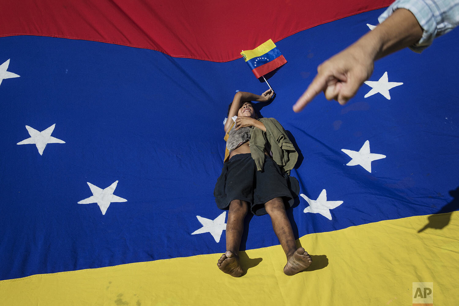  A man points at Oliver Duque, a homeless boy resting on top of a Venezuelan national flag during a demonstration called by opposition politician Juan Guaido, who's urging masses into the streets to force President Nicolás Maduro from power, in Marac