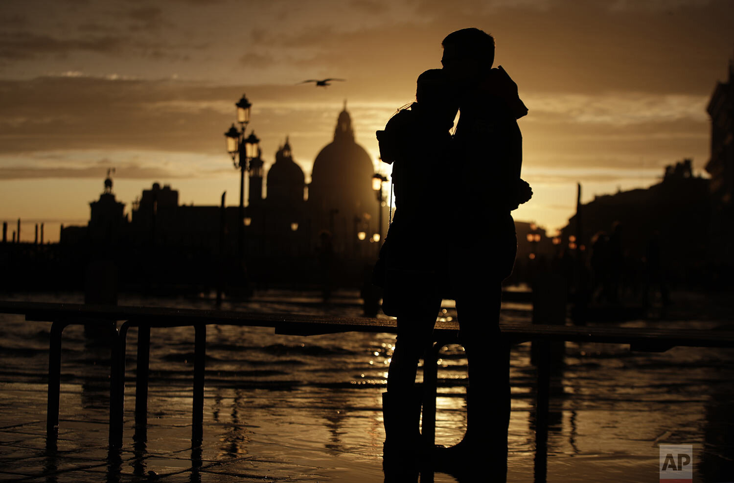  A couple stands in a golden sunset in Venice, Italy, Sunday, Nov. 17, 2019, just hours after an exceptional 1.5 meter tide receded from nearby St. Mark's Square. It was the third flood topping 1.5 meters this week, following Tuesday's 1.87-meter flo