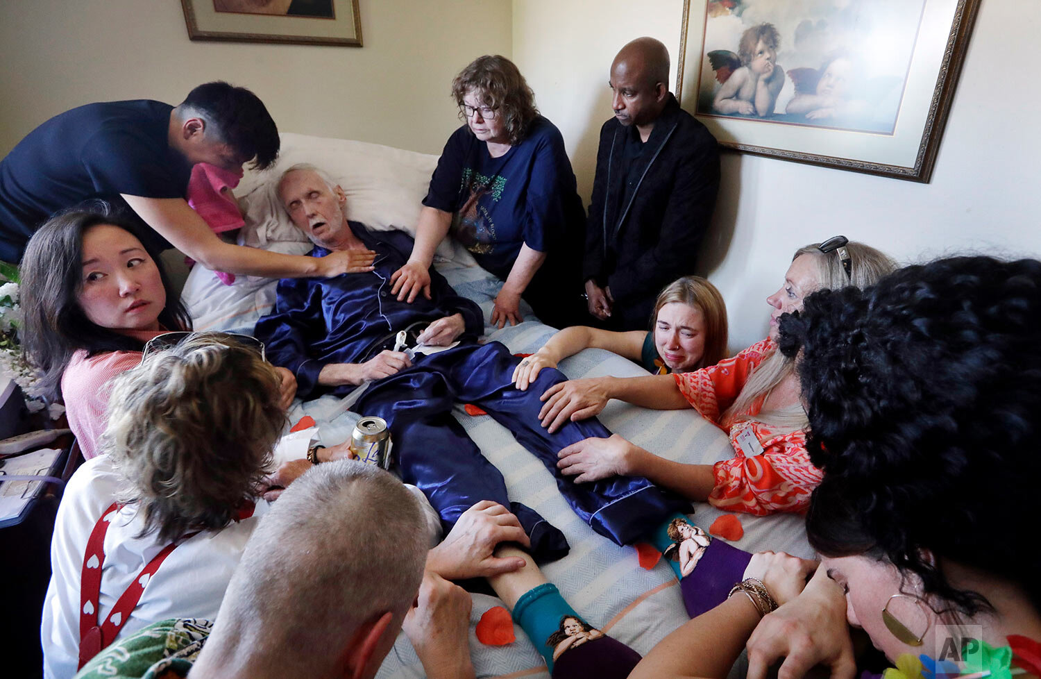  Robert Fuller lies unconscious after plunging drugs that will end his life into his feeding tube as his husband, Reese Baxter, upper left, and friends hold him, in Seattle on May 10, 2019. Fuller was one of about 1,200 people who have used Washingto