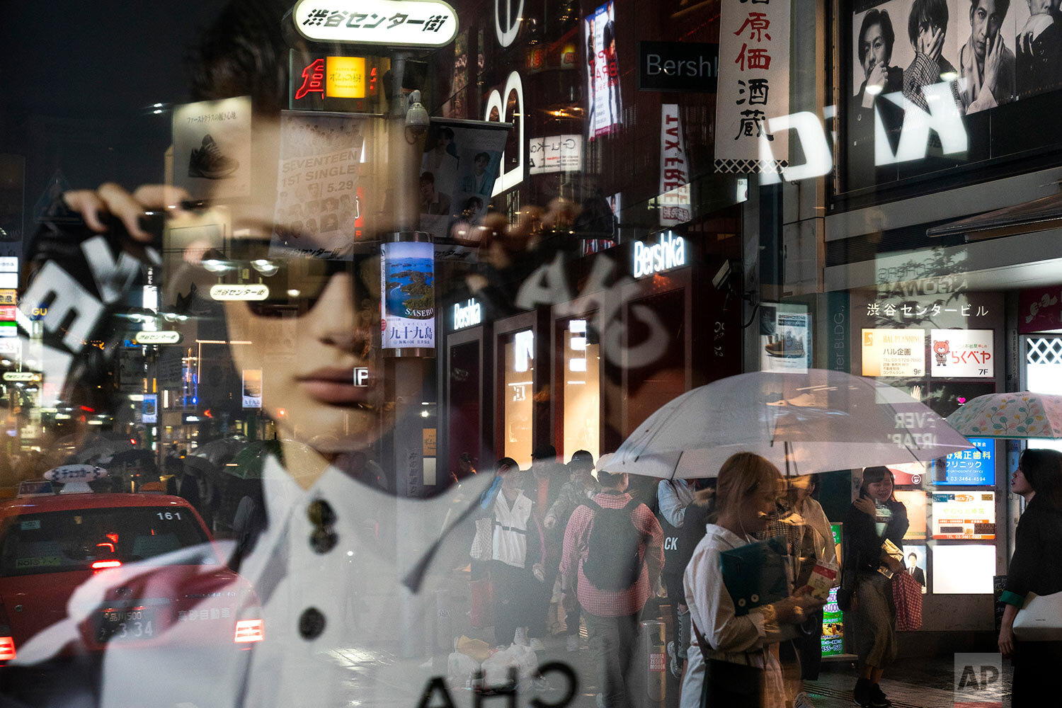  Pedestrians are seen through the reflection of an advertisement in a window as they walk along a busy street in the Shibuya district of Tokyo on June 9, 2019. (AP Photo/Jae C. Hong) 