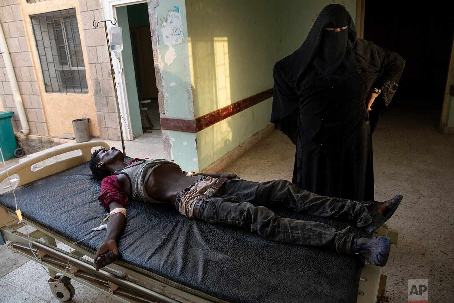  An Ethiopian Tigray migrant who was imprisoned by traffickers for months lies on a gurney accompanied by a nurse at the Ras al-Ara Hospital in Lahj, Yemen, on Aug. 1, 2019. Nurses gave him fluids but he died several hours later. (AP Photo/Nariman El