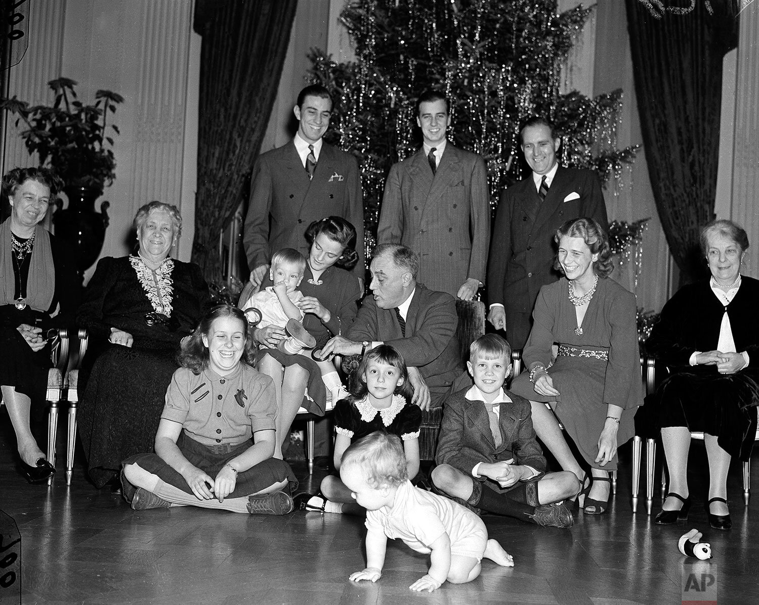  President Franklin D. Roosevelt tries to get the attention of grandchild Franklin Roosevelt III, seated on his mother's lap, as young Johnny Boettiger crawls away in the foreground during a Christmas photo session in the East Room of the White House