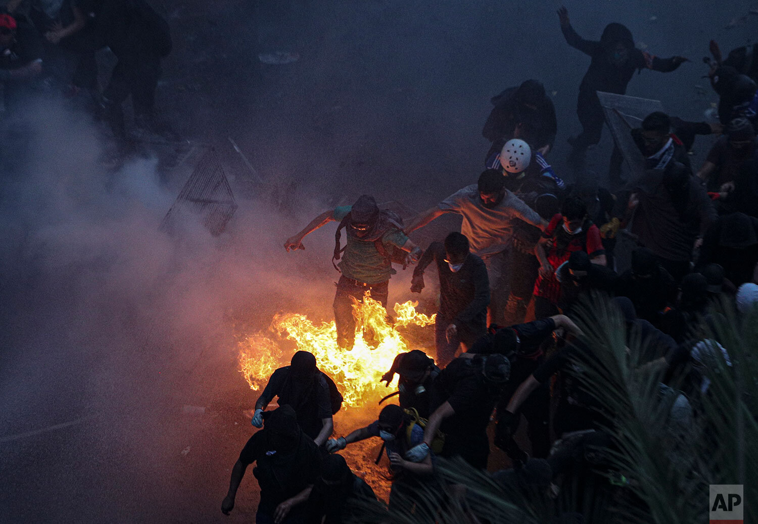  Anti-government protesters jump over a burning barricade as they run from an oncoming police water cannon in Plaza Italia, in Santiago, Chile, Friday, Nov. 8, 2019.  Chile's unrest began last month over a subway fare hike. But it has morphed into a 