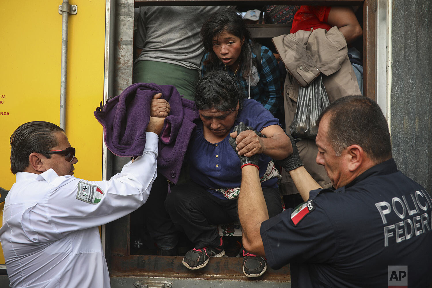  In this Nov. 26, 2019 photo, a federal police officer assigned to the National Guard and a migration agent help a woman off the cargo hold of a truck packed with migrants being smuggled, at an immigration checkpoint where the truck was stopped in Me