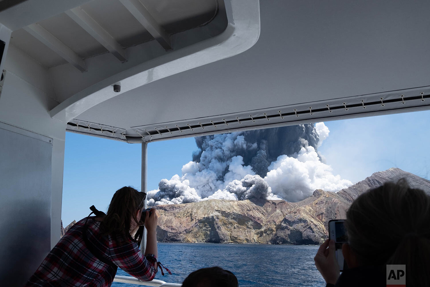  In this photo provided by Michael Schade, tourists on a boat look at the eruption of the volcano on White Island, New Zealand on Monday, Dec. 9, 2019. (Michael Schade via AP) 