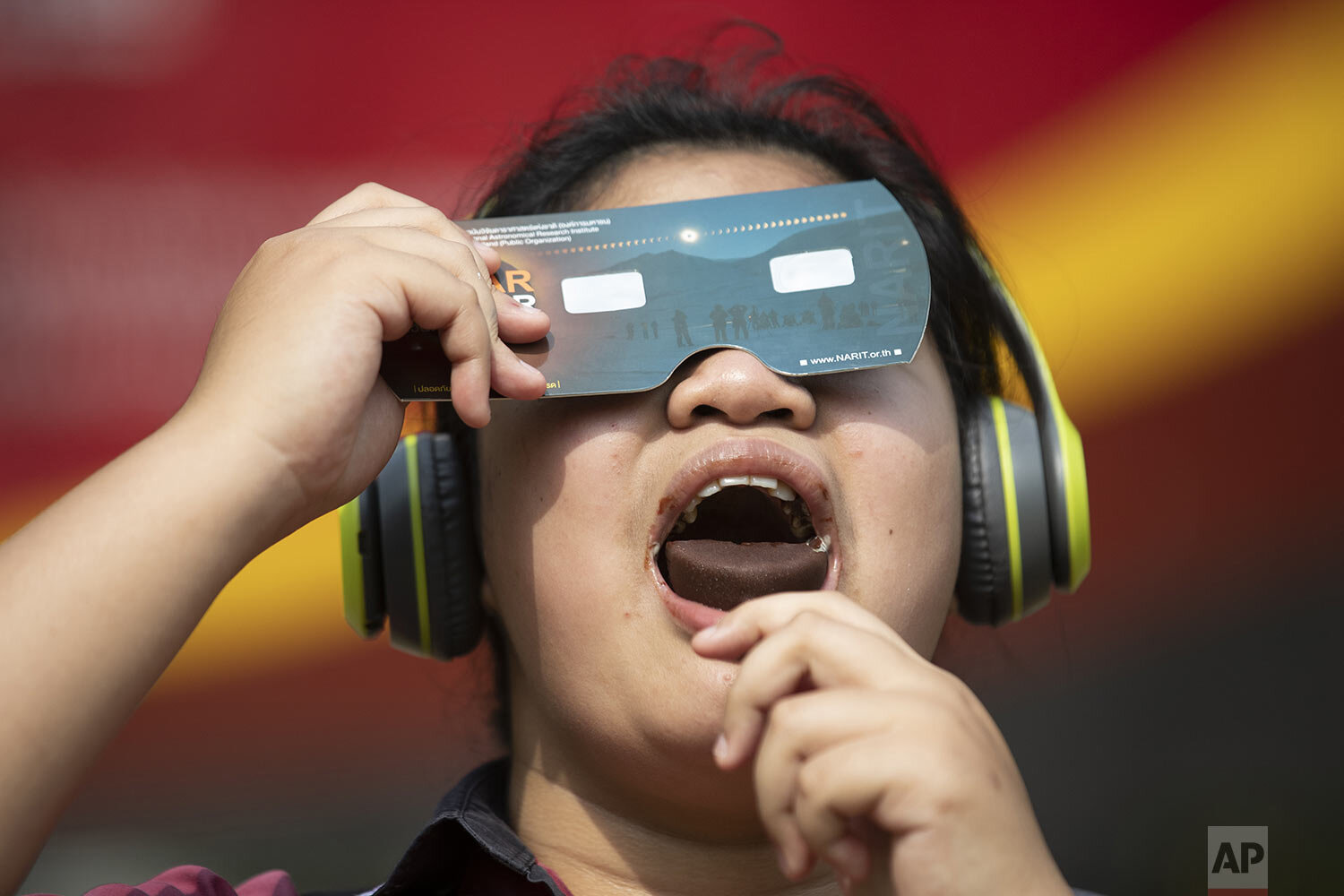  A student holds a special filter to observe a solar eclipse while eating an ice cream treat at a school in Bangkok, Thailand, Thursday, Dec. 26, 2019. (AP Photo/Sakchai Lalit) 