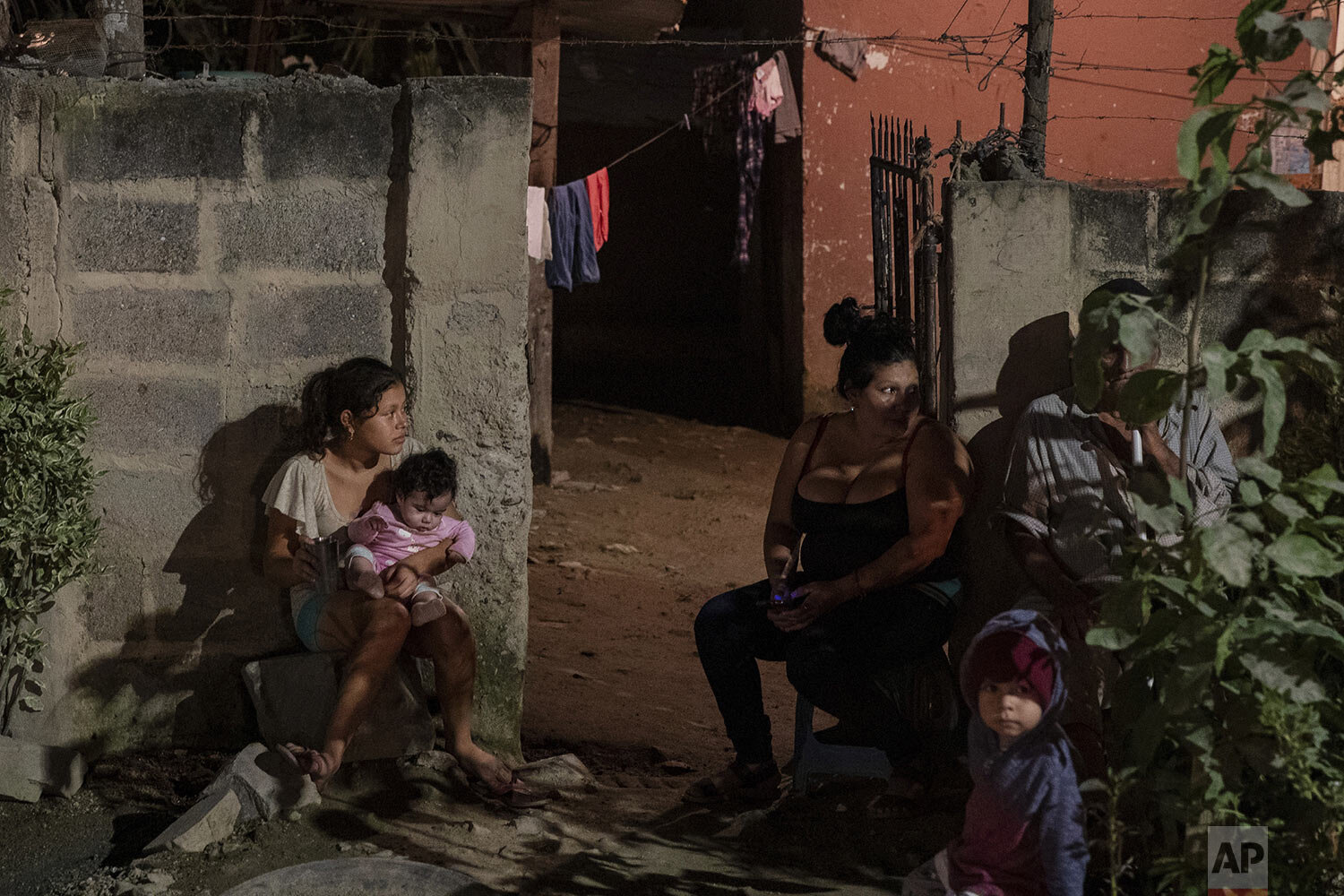  In this photo published in December, a family sits outside their home as forensic workers investigate a body at a crime scene in the Rivera Hernandez neighborhood of San Pedro Sula, Honduras, Nov. 30, 2019. The shifting lines of control of the vario