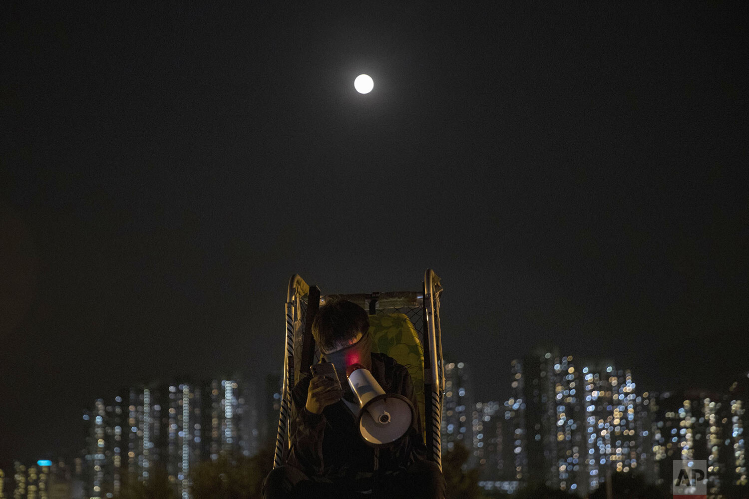  A protester reads out news information over a loud megaphone as a full moon rises over the barricaded bridge into the Chinese University of Hong Kong, in Hong Kong, Wednesday, Nov. 13, 2019. (AP Photo/Ng Han Guan) 