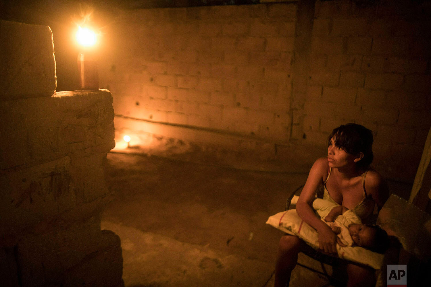  In this May 15, 2019 photo, Jennifer Vejar holds her 2-month-old baby Enmanuel Benitez, illuminated by a torch known in Maracaibo as a "Mechurrio," in reference to the flares that burn excess gases on oil wells, during a black out in Maracaibo, Vene
