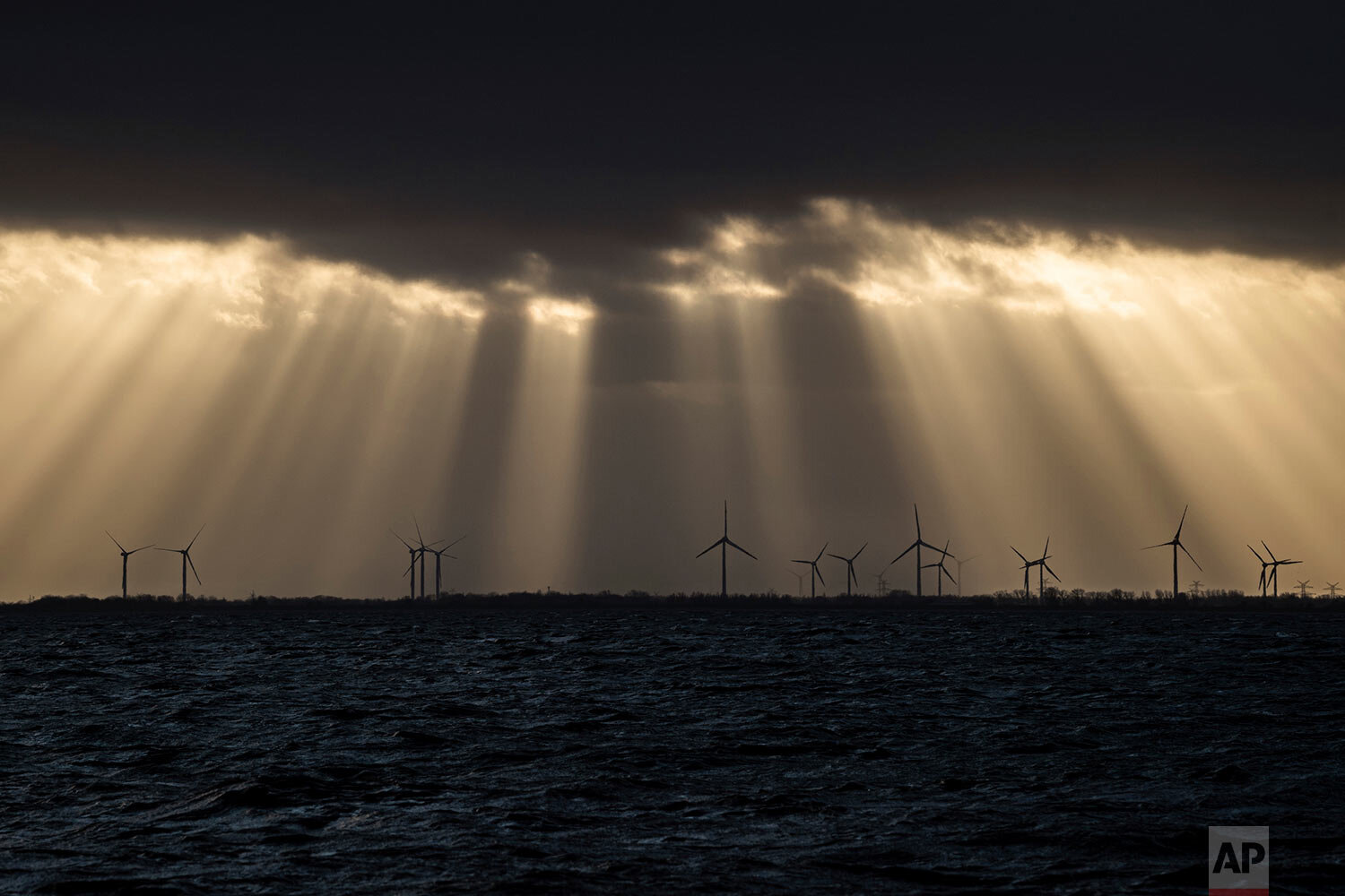  Sunlight breaks through dark clouds shining on a wind farm in Wilhelmshaven, on the North Sea coast of Germany, the evening of Sunday, Dec. 15, 2019. (Mohssen Assanimoghaddam/dpa via AP) 