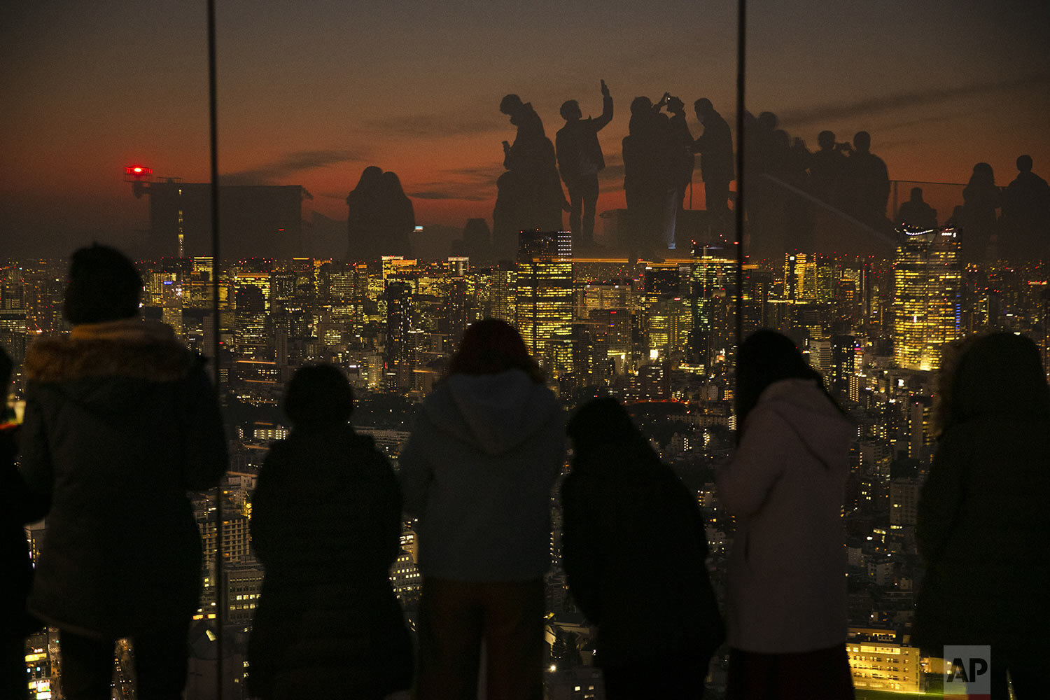  Silhouetted against sunset, visitors are reflected on the glass walls of Shibuya Sky observation deck Monday, Jan. 20, 2020, in Tokyo.  (AP Photo/Jae C. Hong) 