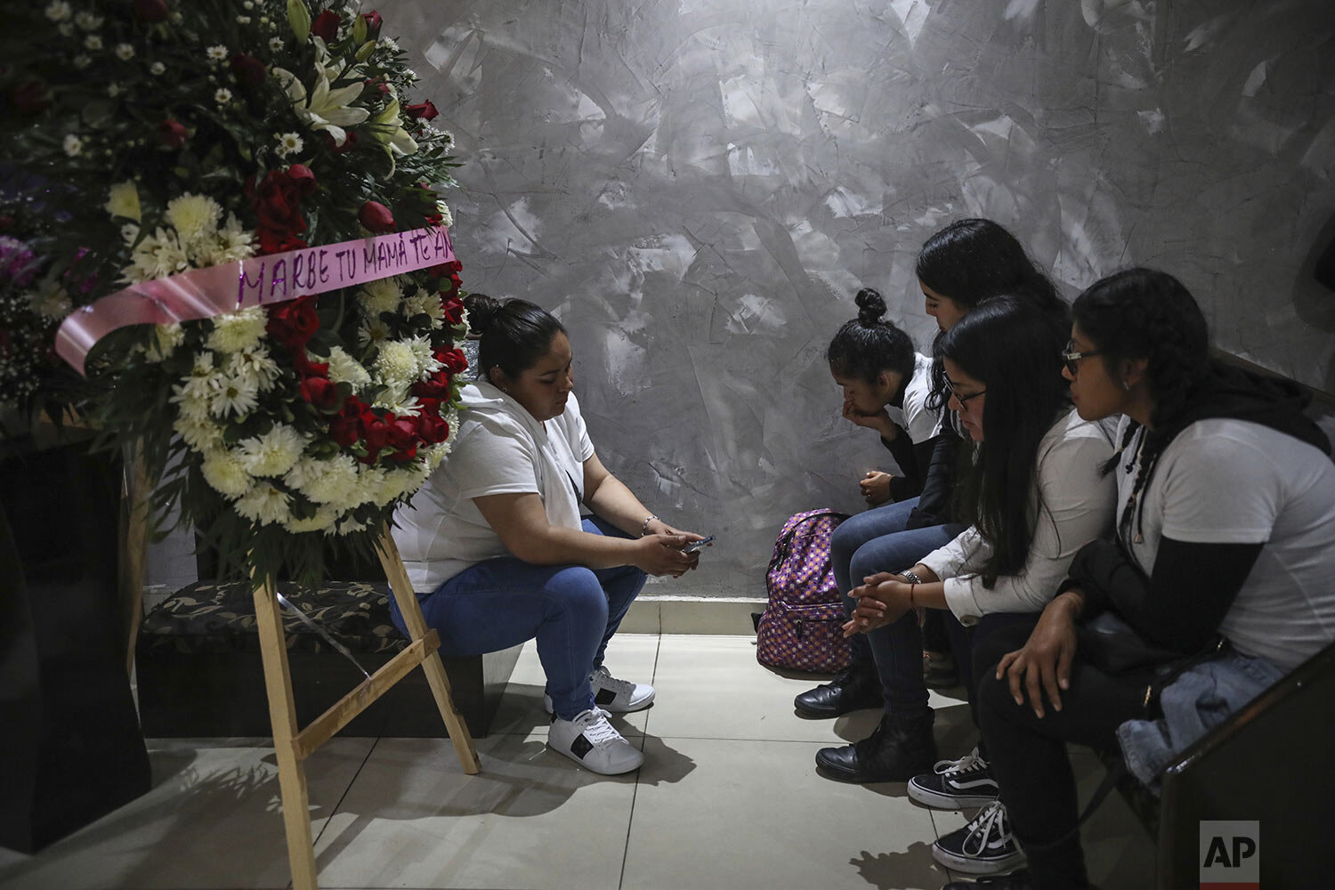  Friends of slain woman Marbella Valdez sit together by a floral arrangement that reads in Spanish "Marbe, your mom loves you," near her coffin during her wake at a funeral home in Tijuana, Mexico, Thursday, Feb. 13, 2020. (AP Photo/Emilio Espejel) 