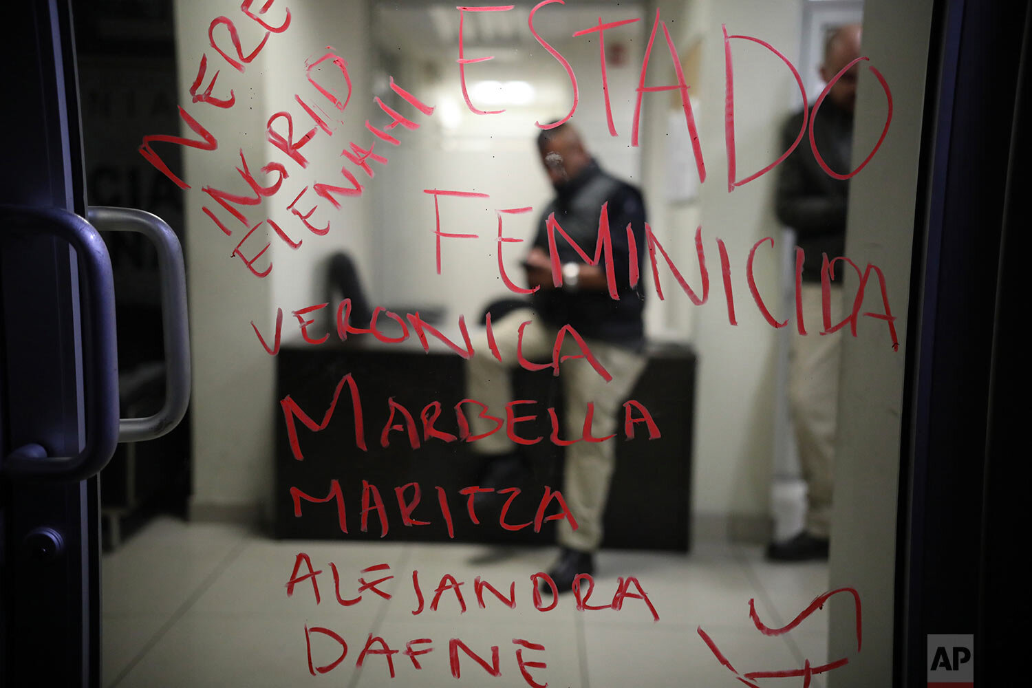  A list of names, written in lipstick, of murdered women and the Spanish words "Femicide state," cover a door at the prosecutor's office where police sit behind, left behind by demonstrators protesting gender violence in Tijuana, Mexico, Saturday, Fe