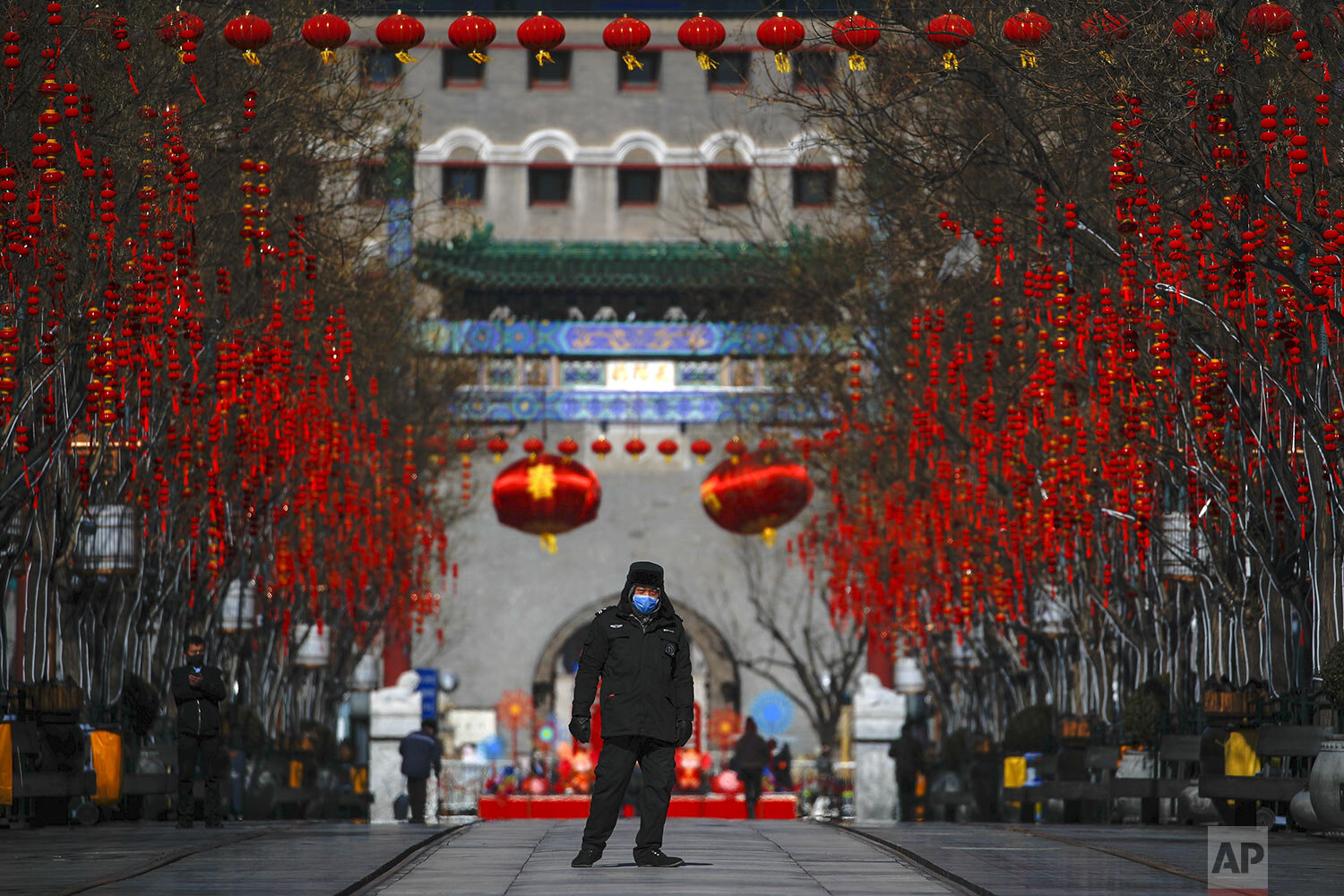 A security guard wearing a face mask walks through a quiet main Qianmen Street, a popular tourist spot, in Beijing, Sunday, Feb. 16, 2020. (AP Photo/Andy Wong)